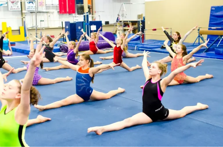 This image shows a gymnastics class filled with young athletes practicing their splits on a blue mat at Excel Gymnastics Academy.