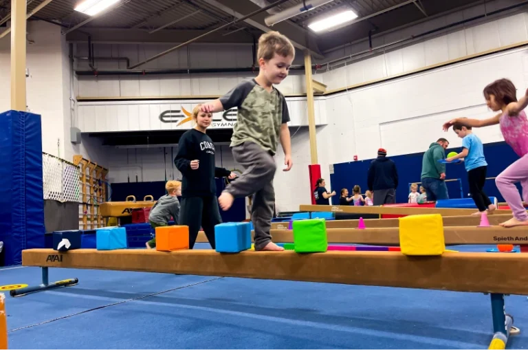This image shows children participating in a structured gymnastics class designed for balance and coordination training at Excel Gymnastics Academy