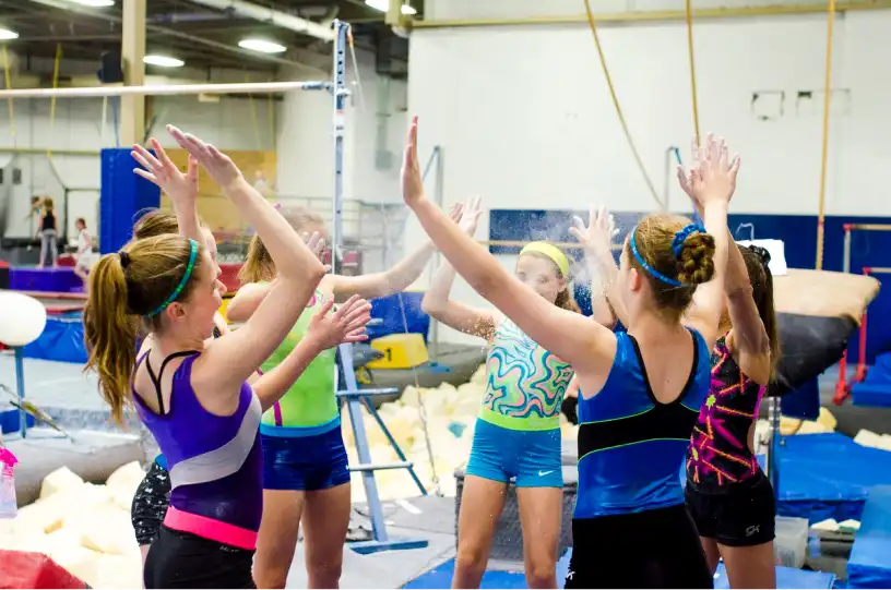 This image shows a group of young gymnasts celebrating a successful training session with high-fives at Excel Gymnastics Academy.
